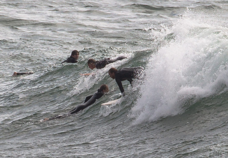 Surfers paddling and riding waves in wetsuits.