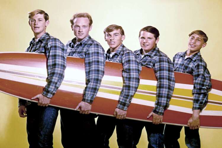 Classic photo of The Beach Boys holding together a yellow and red surfboard